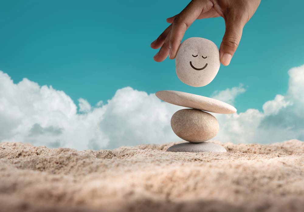 Making a wellness person with rocks and smiling face on the top one, sitting on sand.